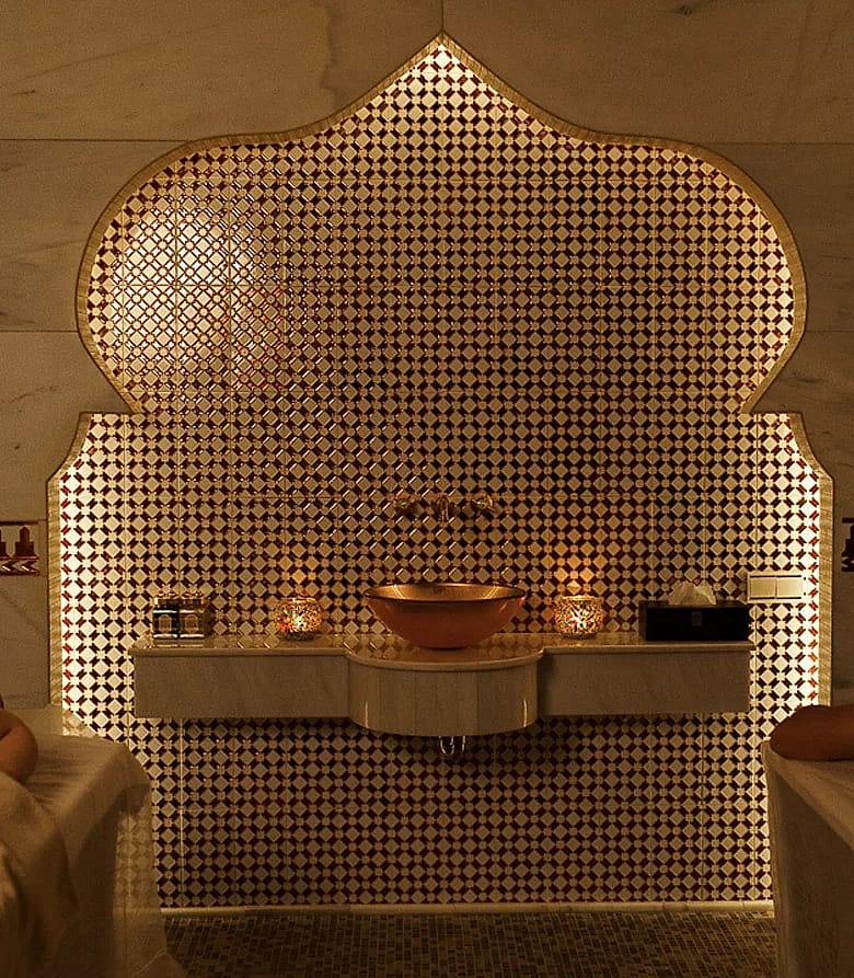 Two guests resting on marble beds in front of a glowing tiled arch